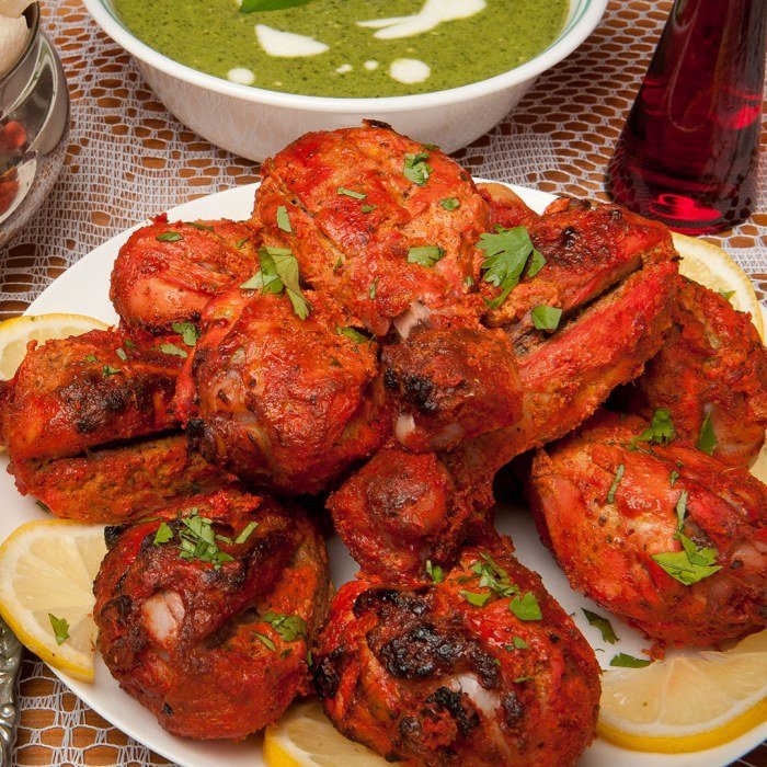 Tandoori piščanec na žaru z zlato rjavo skorjico, postrežen z naan kruhom in limono.